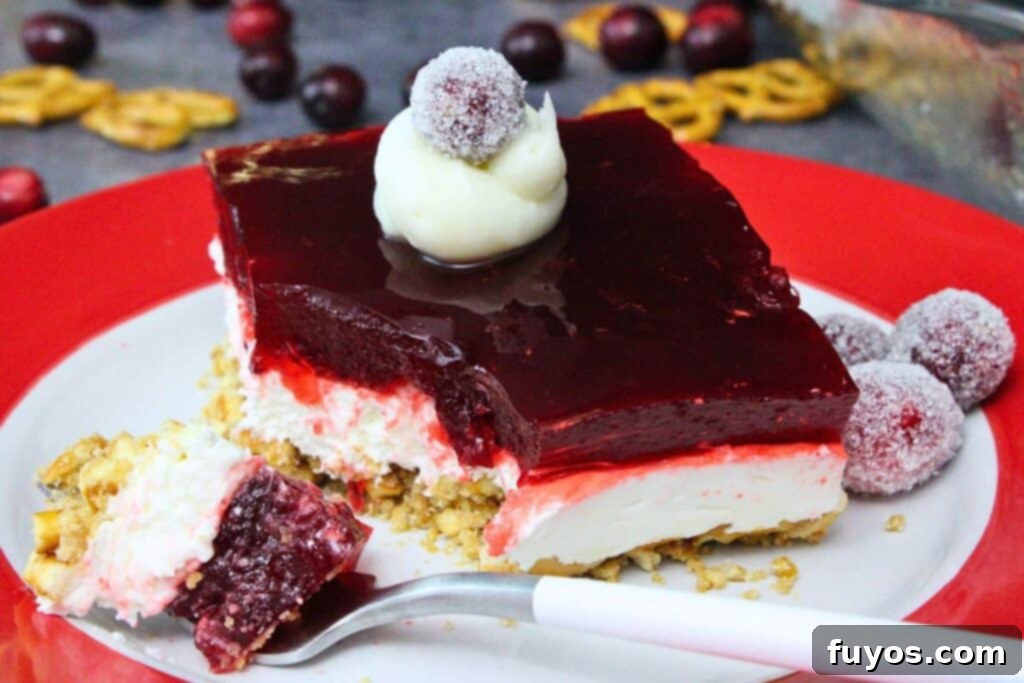 closeup view of a cranberry pretzel salad square on a red and white plate with a fork cutting through the dessert