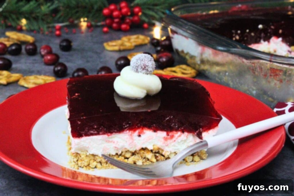 cranberry pretzel salad square topped with sugared cranberry and a fork to the side amidst holiday decor