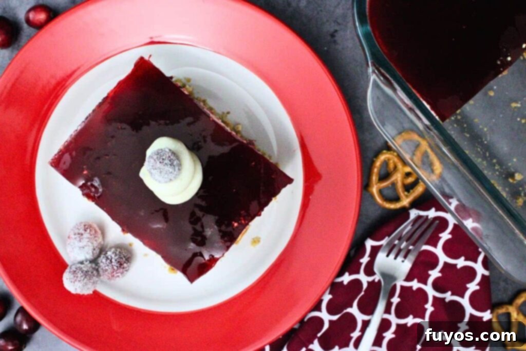 overhead view of cranberry pretzel salad square on a red and white plate with cool whip dollop and sugared cranberries