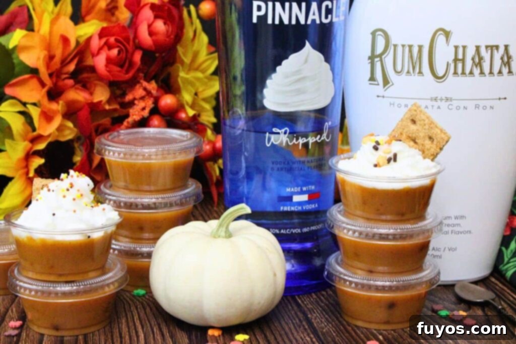 Several pumpkin pie pudding shots with whipped cream and sprinkles arranged in front of liquor bottles