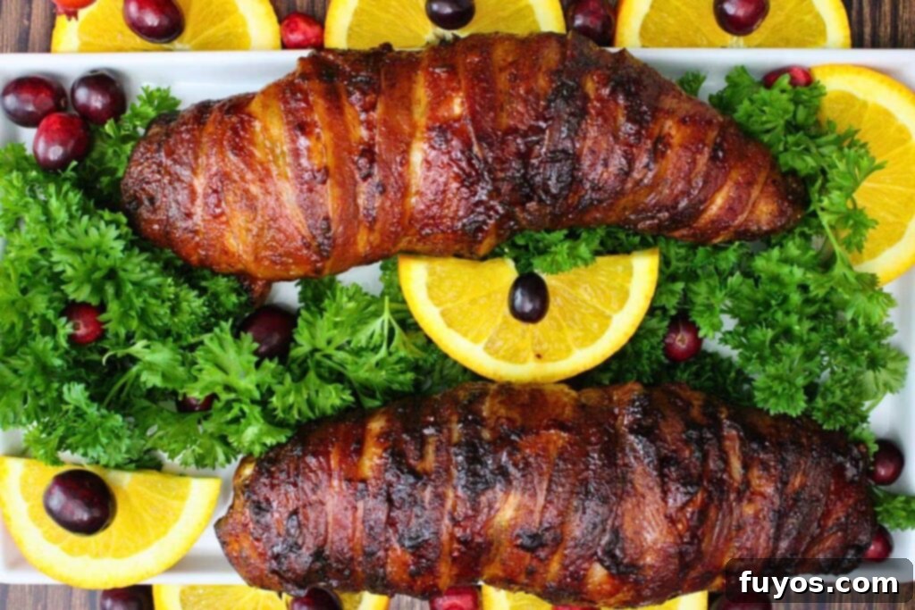 Easy Air Fryer BBQ Bacon Wrapped Turkey Tenderloin 8 overhead view of two bacon wrapped turkey tenderloins with bbq sauce on a platter with parsley, orange, and cranberry
