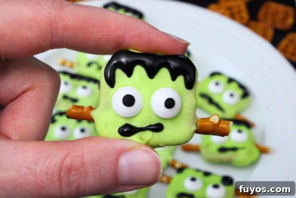 holding up a green frankenstein pretzel showing googly candy eyes and icing face