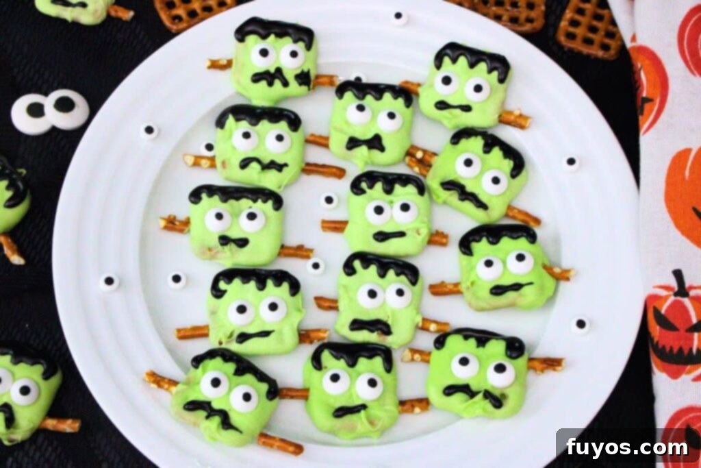 green frankenstein pretzels with googly candy eyes on a plate surrounded by halloween napkin on a dark counter