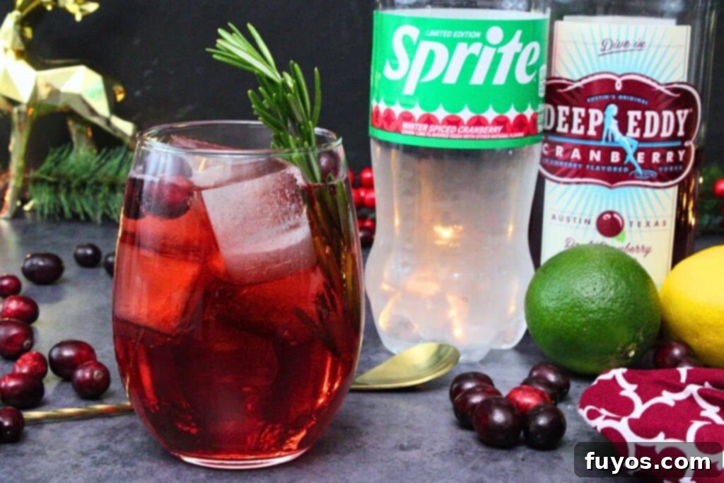 cranberry vodka spritzer next to sprite and vodka bottle amidst holiday pine sprigs and cranberries