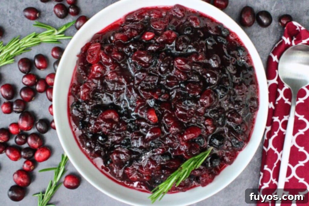 Overhead view of glistening microwave cranberry sauce in a white shallow serving bowl, garnished with fresh cranberries and a sprig of rosemary