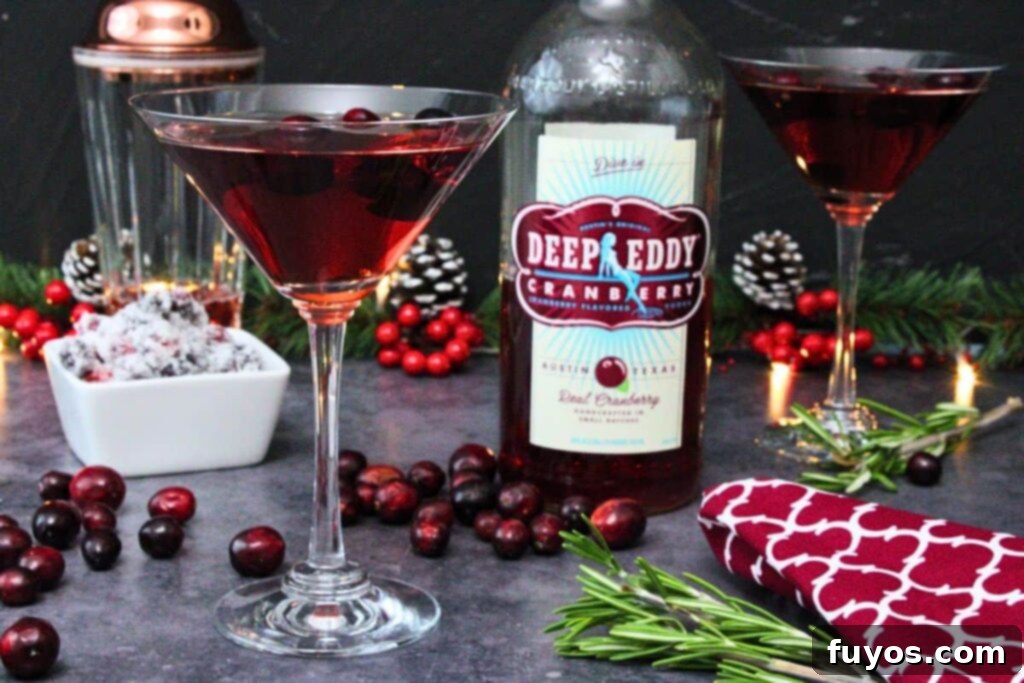 Effortless Holiday Cranberry Martini Vodka Drink 8 Two cranberry martinis with vodka bottle in the center surrounded by fresh cranberries and pine sprigs.