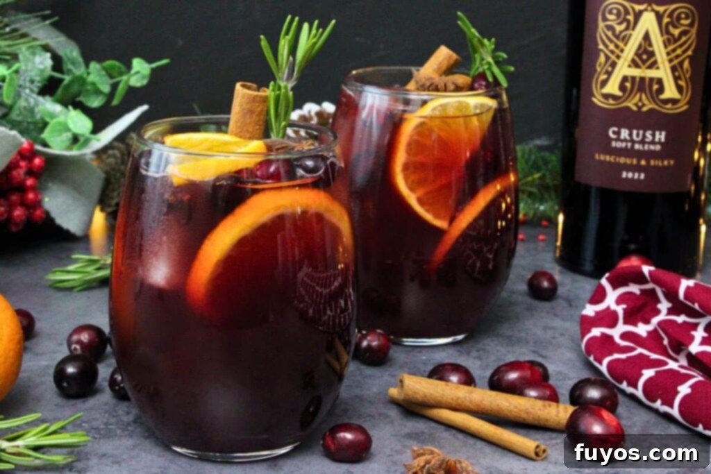 Two glasses of rich, dark red cranberry sangria, elegantly garnished with fresh orange slices and aromatic rosemary sprigs, set against a backdrop of a wine bottle, ready to be served.