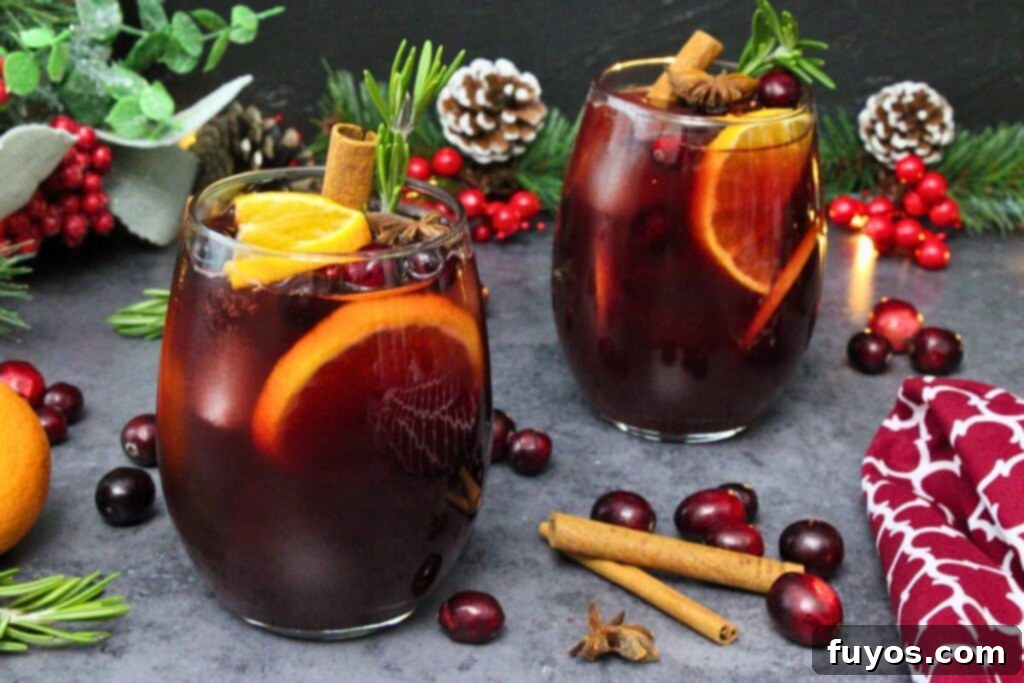 Two exquisite cranberry sangria drinks, artfully garnished with fresh orange slices, a sprig of fragrant rosemary, and a warming cinnamon stick, set amidst elegant holiday decorations and scattered fresh cranberries, showcasing festive presentation.