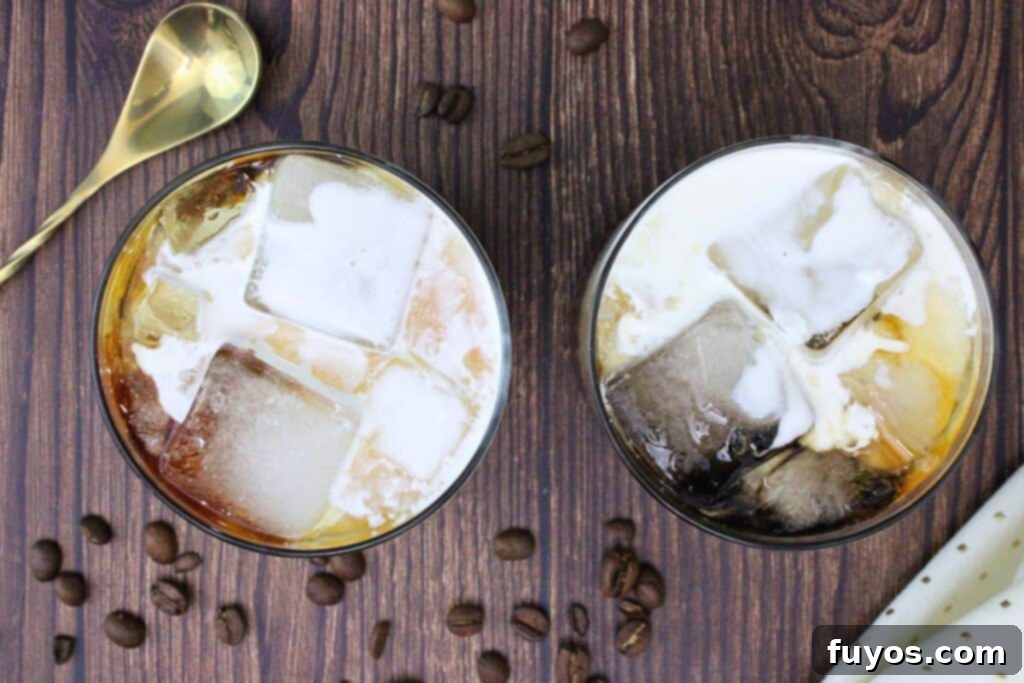 overhead view of two white russian drinks on a wooden counter with coffee beans and gold stirrer
