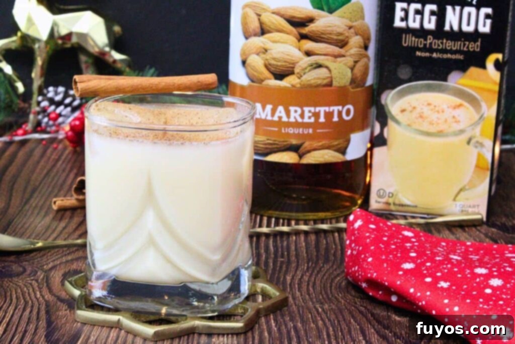 Amaretto Eggnog in a lowball glass with a cinnamon stick, liquor bottle, and eggnog carton