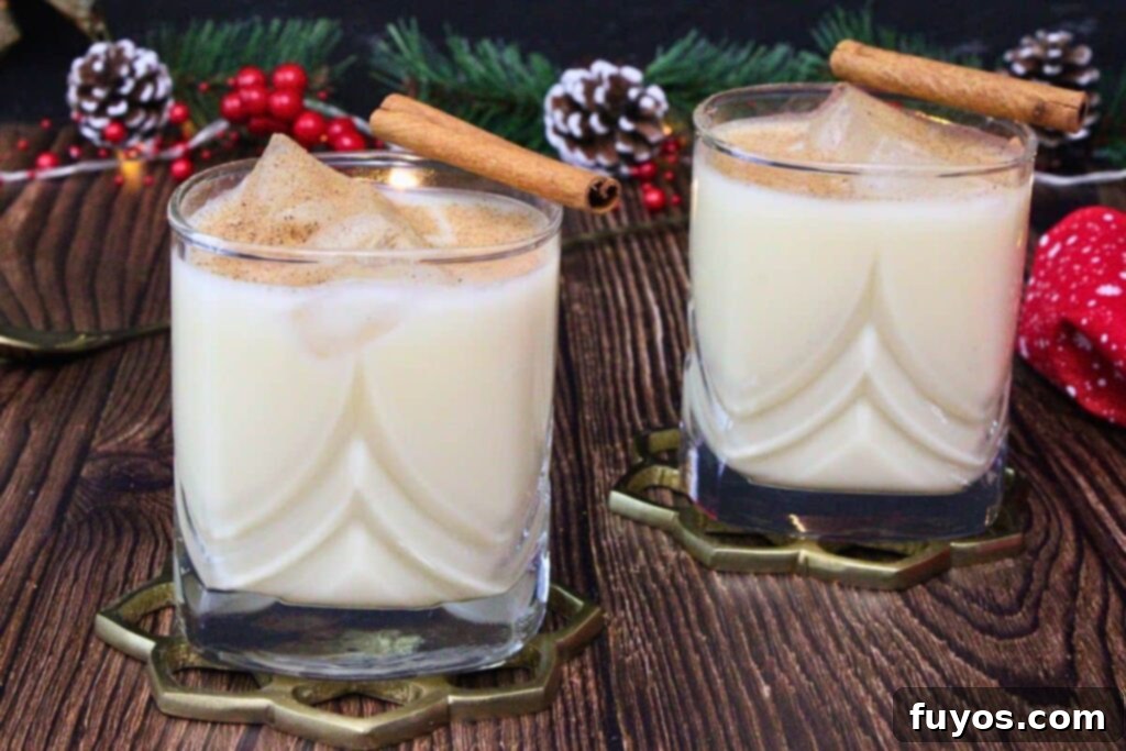 Two amaretto eggnog drinks dusted with nutmeg and a cinnamon stick surrounded by winter decor