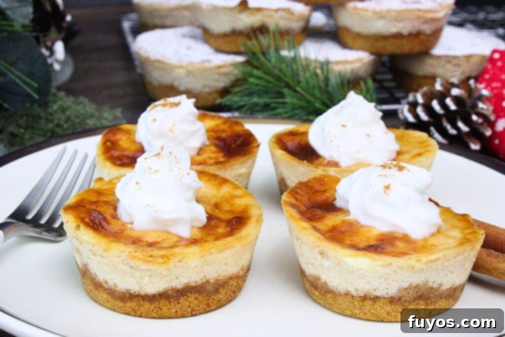 Four mini eggnog cheesecakes with a swirl of whipped cream on a plate next to a for and winter decorations