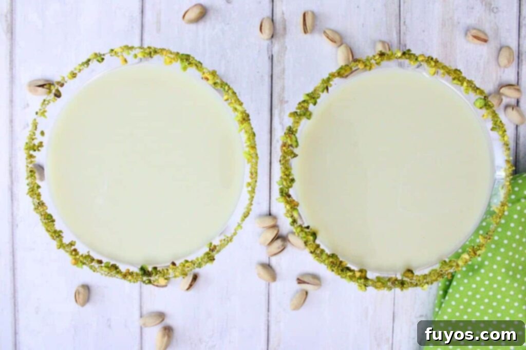 overhead view of two pistachio martinis rimmed with nuts on a white wooden counter