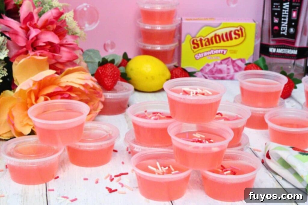Pink Whitney Jello shots spread across a white wooden table with flowers, strawberries, and lemons