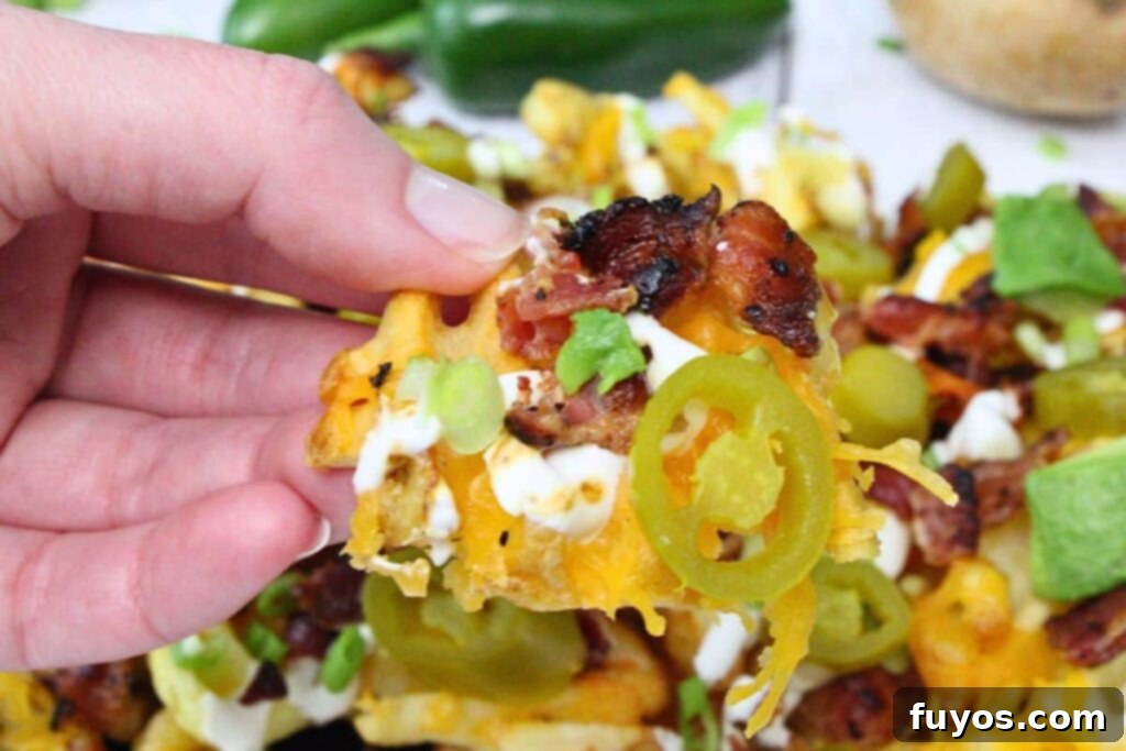 Holding up a waffle nacho fry topped with melted cheese, bacon, sour cream, avocado, and jalapeno