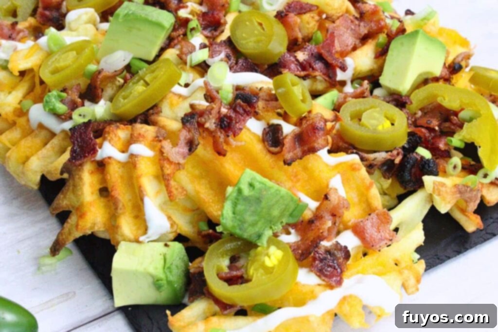 Closeup view of loaded air fryer waffle fry nachos topped with melted cheese, bacon, sour cream, avocado, and jalapeno