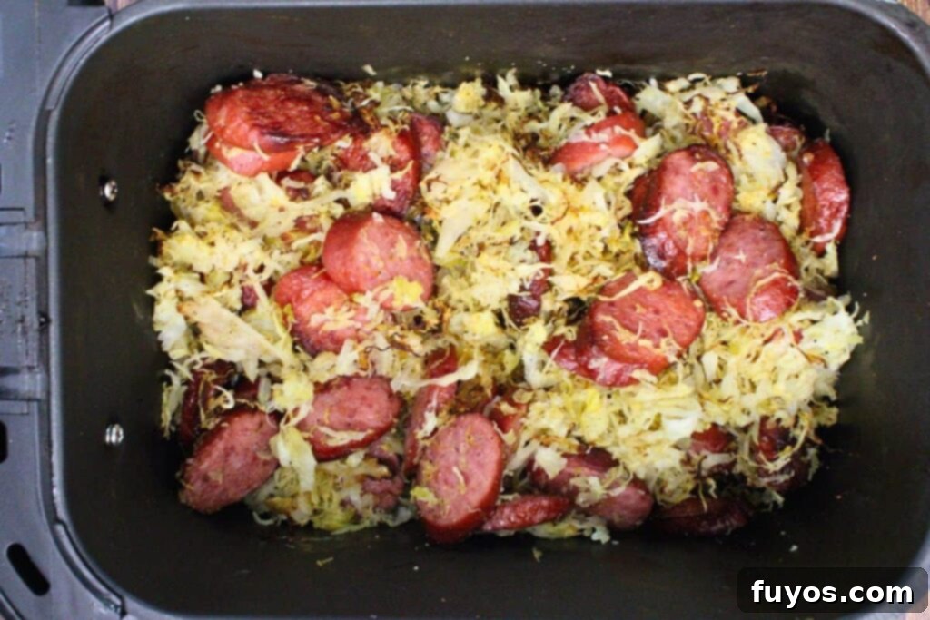 Adding seasoned sauerkraut to kielbasa in air fryer basket