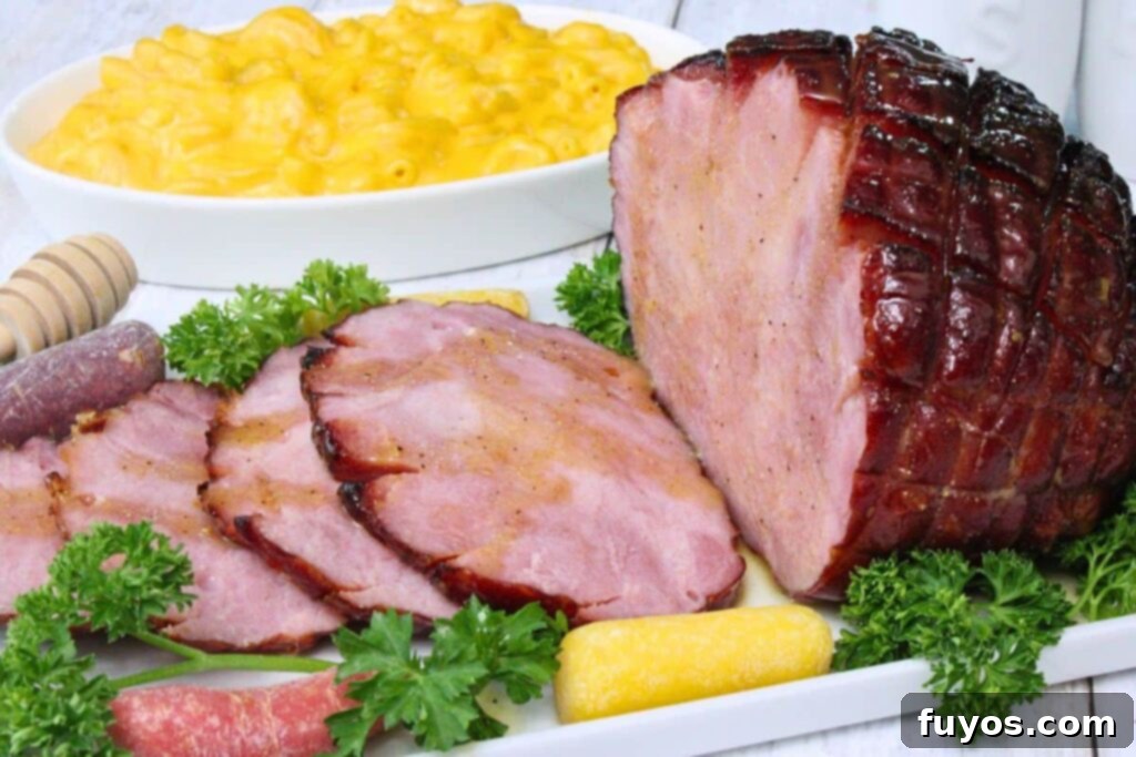 Air fryer hot honey glazed small ham on a plate with slices cut off on a bed of parsley and carrots with mac and cheese in the back
