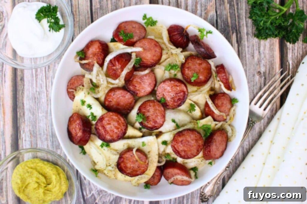 Overhead view of kielbasa and pierogies in a bowl with onions and parsley on a wooden table with side of sour cream and mustard